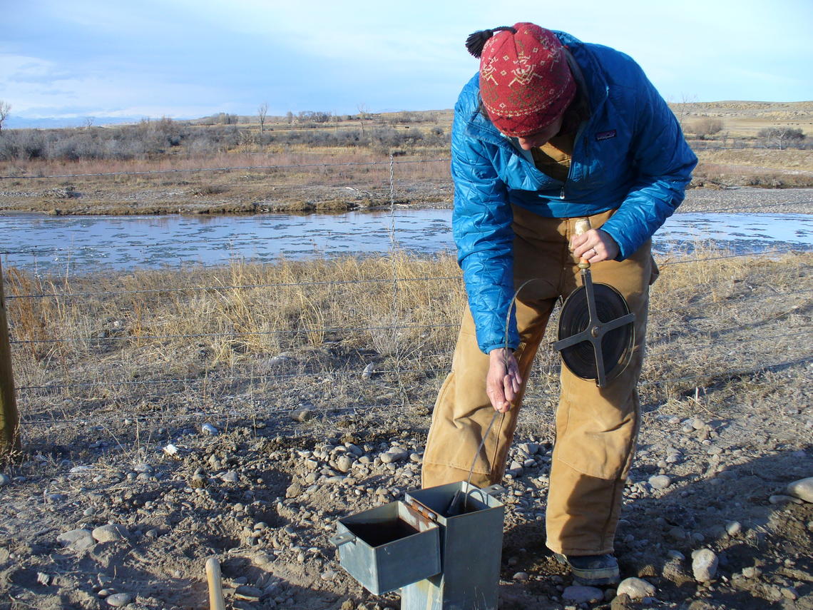 A photo of a person lowering an instrument into a groundater well.