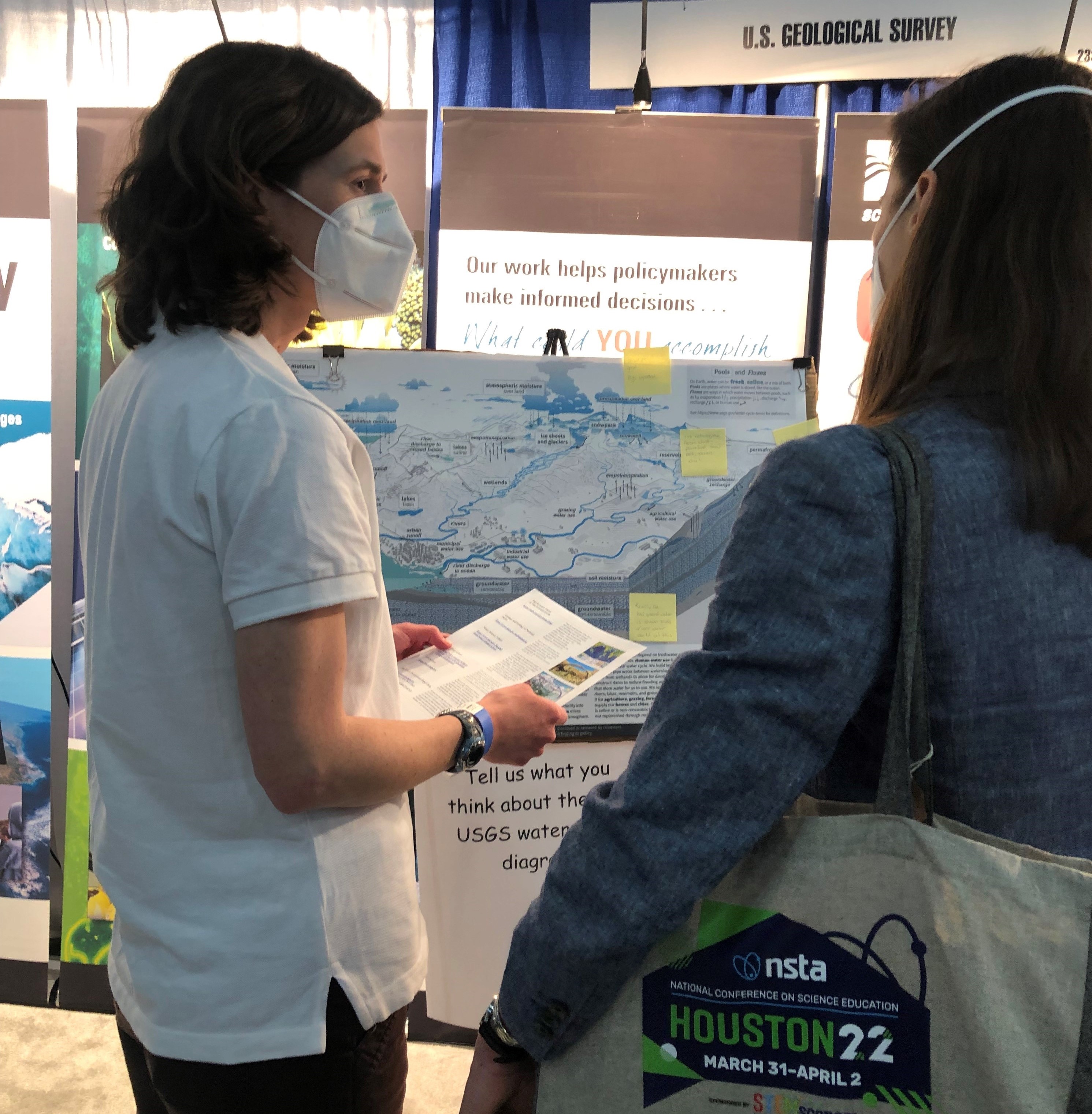 A USGS employee stands in front of a poster of the new water cycle diagram while she talks with a confererence attendee.