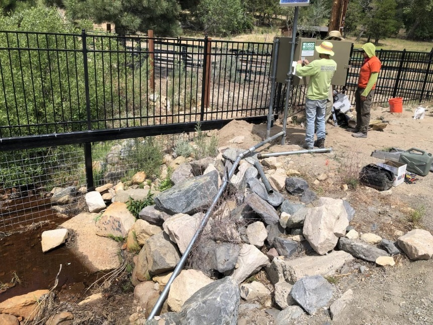 A photograph of two people repairing instrumentation on a stream bank. No data will be transmitted during this activity and a web flag can be applied to data during this time period.